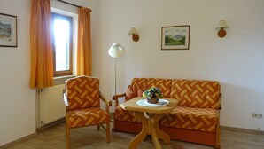 A living room with a sofa, two armchairs, a table with a vase, a floor lamp, and two wall-mounted lamps. - Neureuth - House Schußmann (Tegernsee)