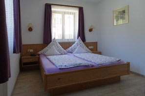 A single bed with a wooden frame, two bedside tables, a window with curtains, and a wall-mounted lamp. - Neureuth - House Schußmann (Tegernsee)