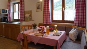 A cozy dining area with a table set for two, a sofa, and a window with curtains. - Neureuth - House Schußmann (Tegernsee)