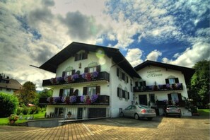 Un bâtiment à deux étages doté de balcons ornés de fleurs, une enseigne indiquant « Gästehaus Meren », et une allée pavée.