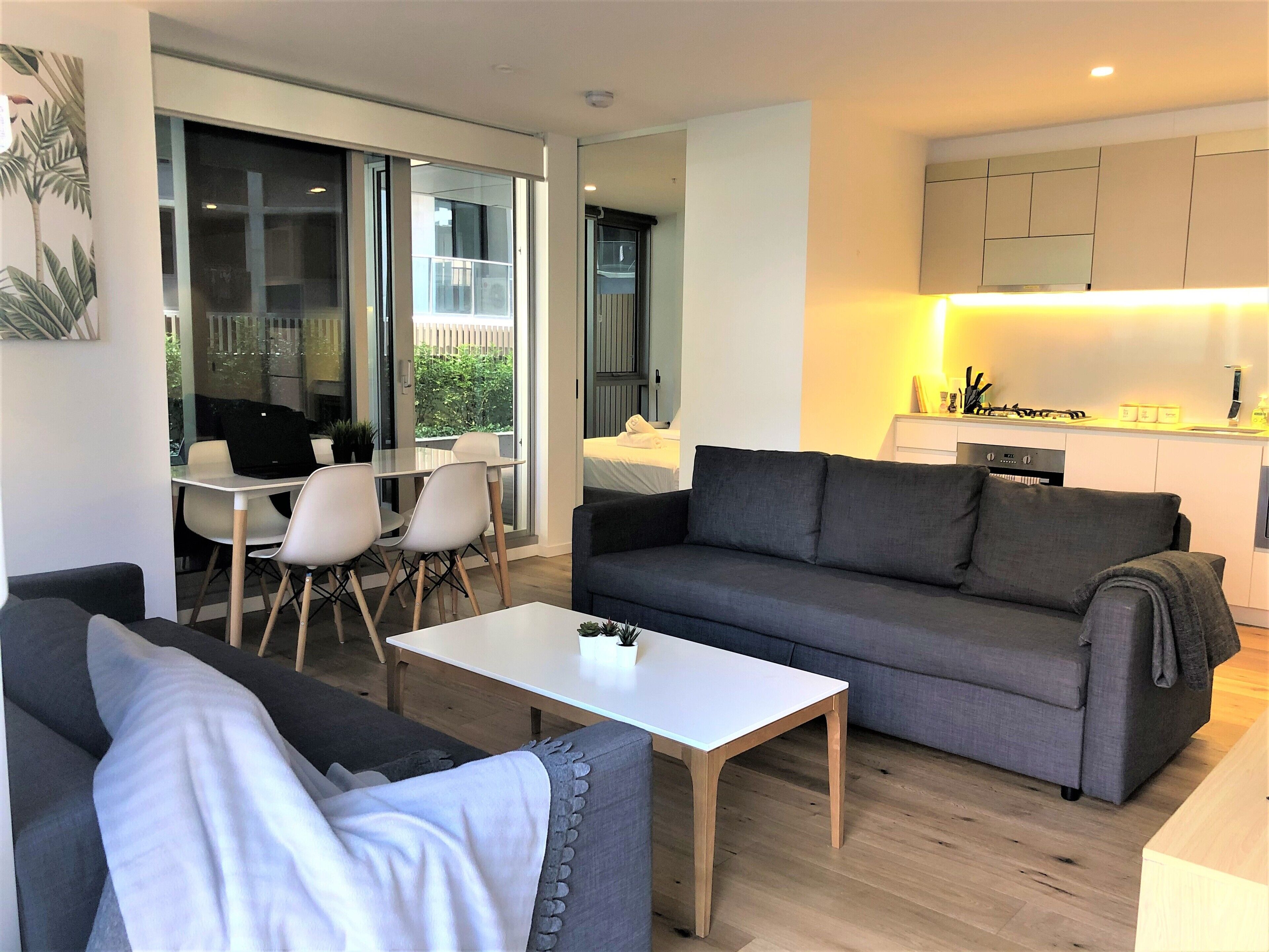 A modern living room with a grey sofa, a white coffee table, and a dining area with white chairs and a glass table.