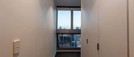 A narrow hallway with a carpeted floor, white walls, and a large window at the end.