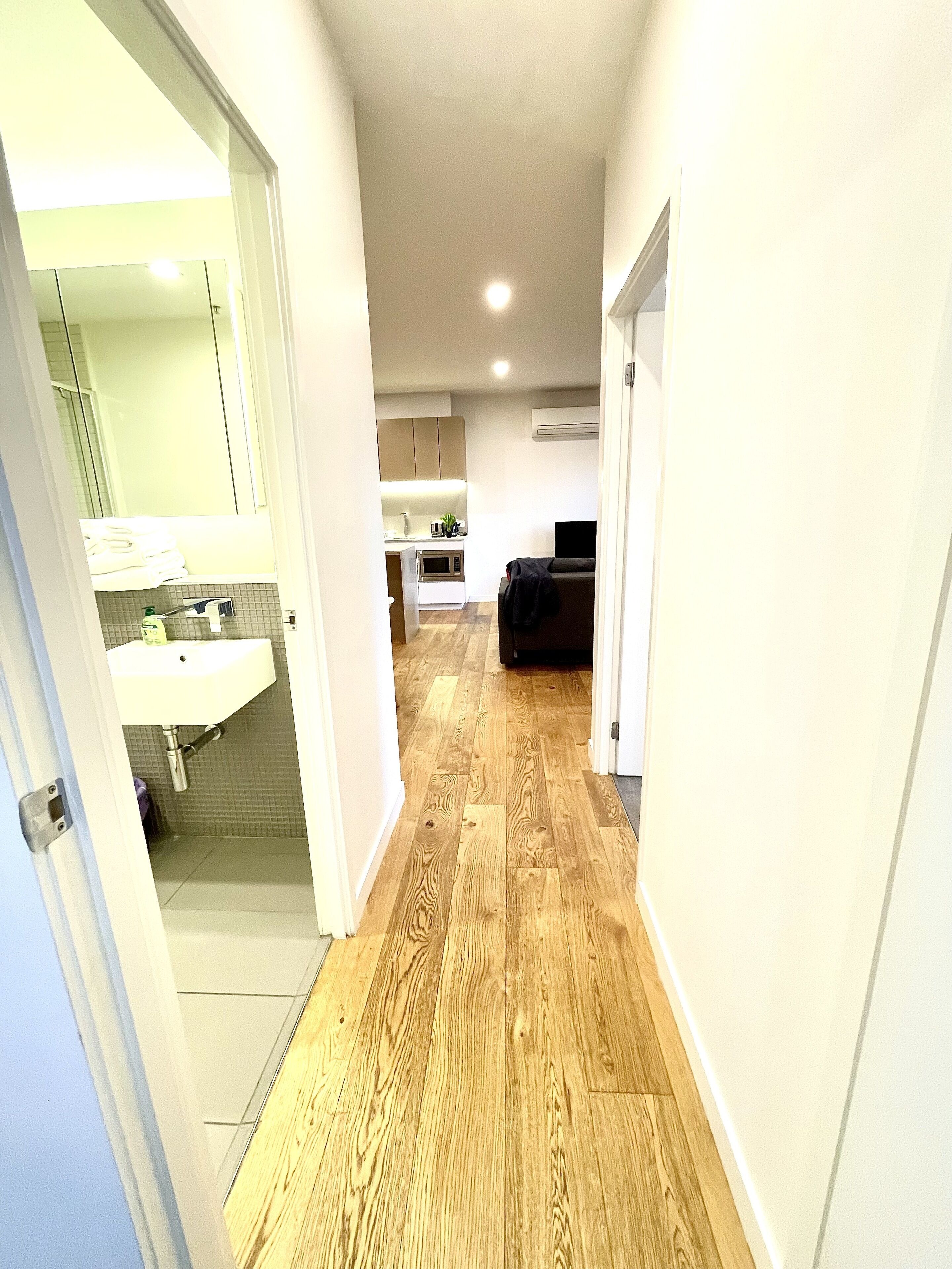Un pasillo estrecho con piso de madera que conduce a una cocina con gabinetes blancos y un horno empotrado.