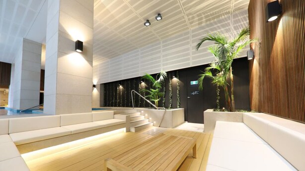 Un espace intérieur moderne comprenant un banc en bois, un escalier et un espace d’accueil agrémenté de plantes.