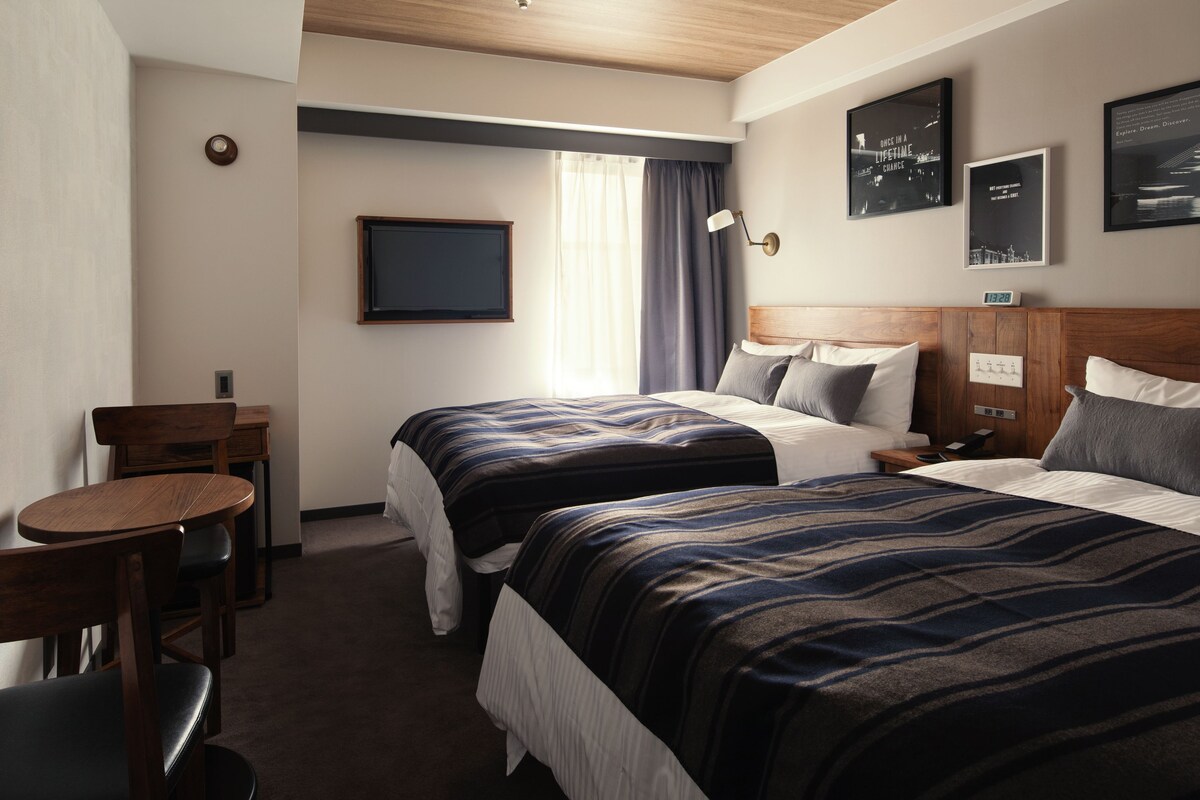 Habitación de hotel con dos camas, un escritorio, una silla y un televisor.