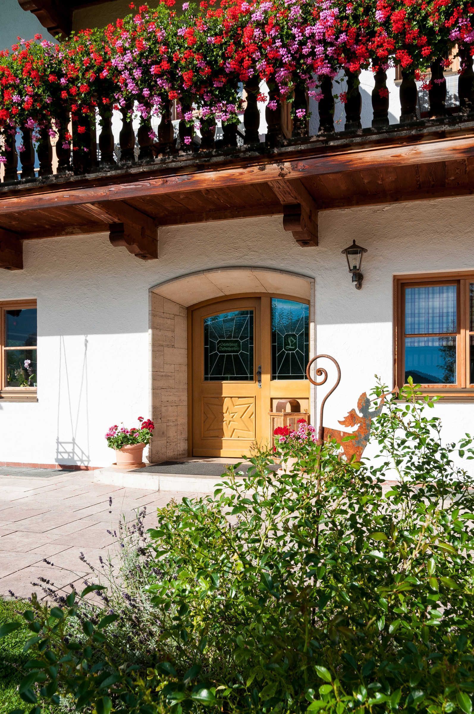 Ein traditionelles Chalet mit einem hölzernen Balkon, der mit bunten Blumen geschmückt ist, einer einladenden Holztür und einem kleinen Garten.