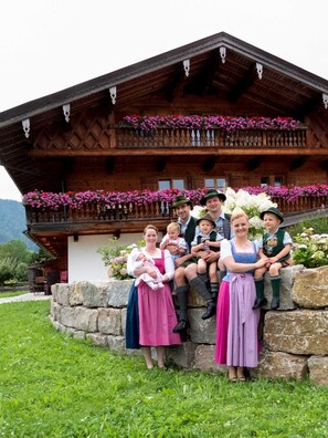 Ein Holzgebäude mit einem Balkon, der mit Blumen geschmückt ist, eine Steinmauer und eine Rasenfläche davor.