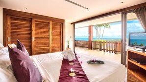 Une chambre d’hôtel avec un grand lit, une armoire en bois et un balcon donnant sur l’océan.