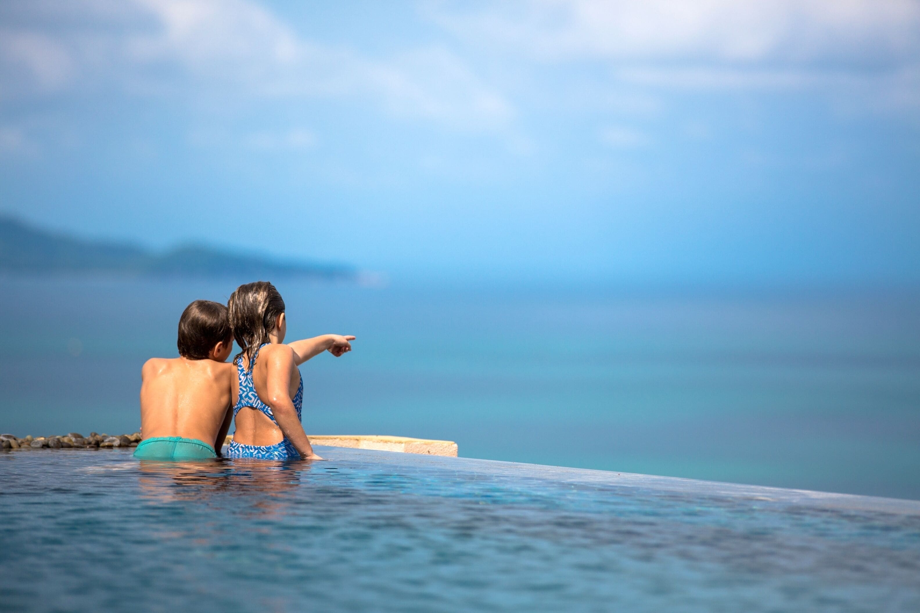 Two people sitting by a poolside with a view of the sea.