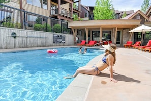 A swimming pool with a lounge area, red chairs, and a covered seating area.