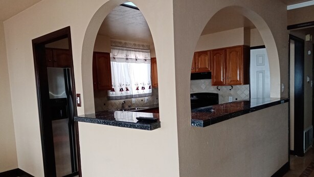 A kitchen with a refrigerator, sink, and wooden cabinets. There are arched doorways and a tiled floor. - House with Panoramic view 15 mins to SF airport (Daly City)
