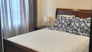 A bedroom with a wooden bed, a nightstand with a lamp, and a window with curtains. - House with Panoramic view 15 mins to SF airport (Daly City)