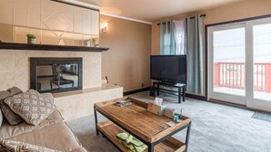 A living room with a fireplace, a sofa, a coffee table, a television, and a balcony with a railing. - House with Panoramic view 15 mins to SF airport (Daly City)