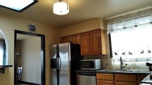 A compact kitchen with wooden cabinets, a stainless steel refrigerator, a microwave, and a dishwasher. - House with Panoramic view 15 mins to SF airport (Daly City)