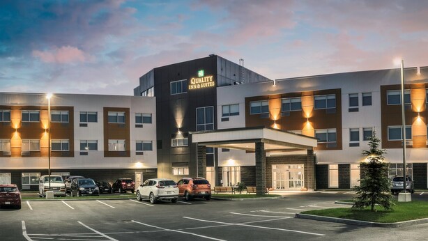 Een meerlaags hotel met een modern design, met een parkeerplaats met meerdere auto's, een overdekte ingang en een goed verlichte gevel.
