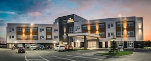 A multi-story hotel with a modern design, featuring a parking lot with several cars, a covered entrance, and a well-lit facade. - Quality Inn & Suites (Mont Joli)