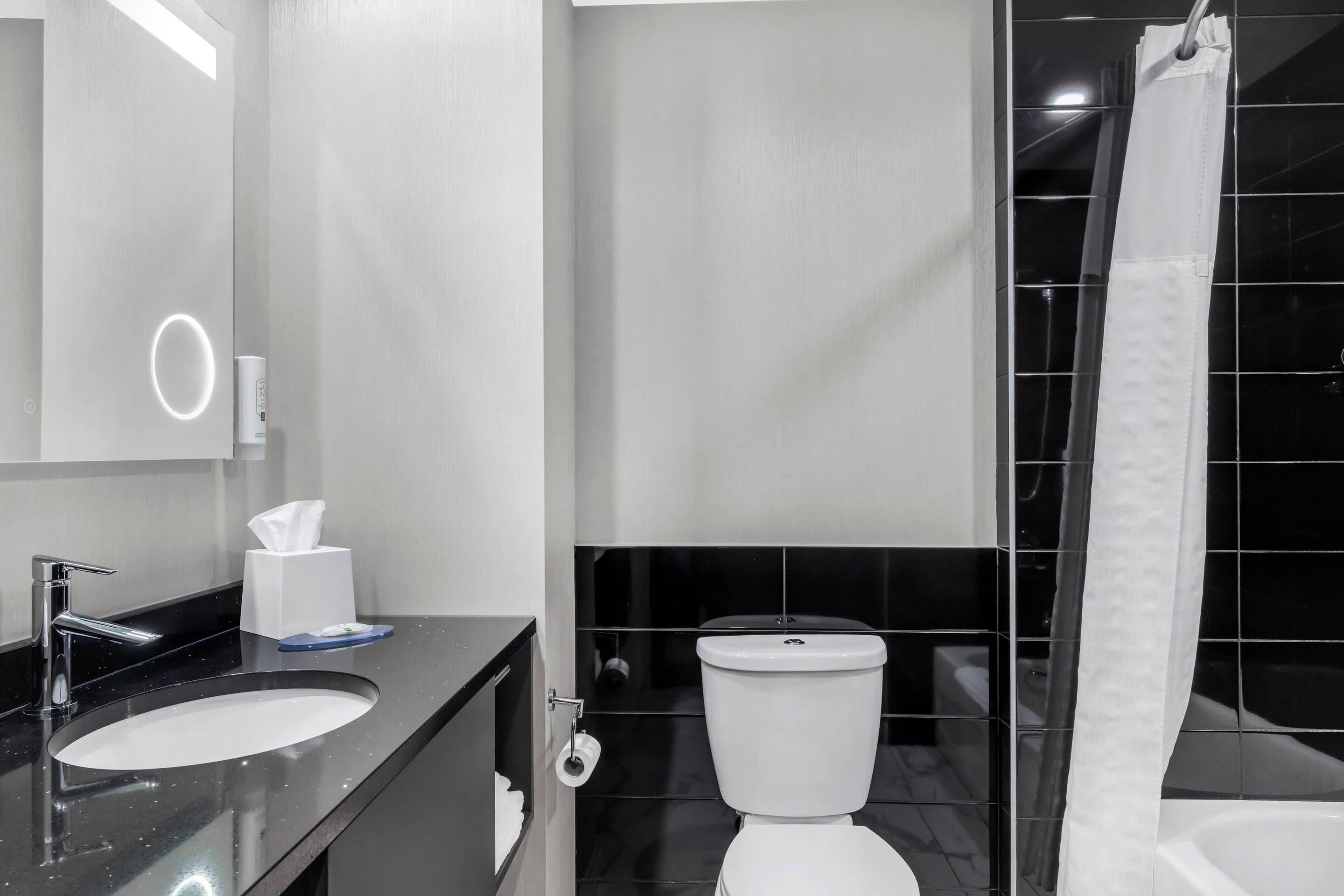 A modern bathroom with a black countertop sink, a white toilet, and a shower curtain.