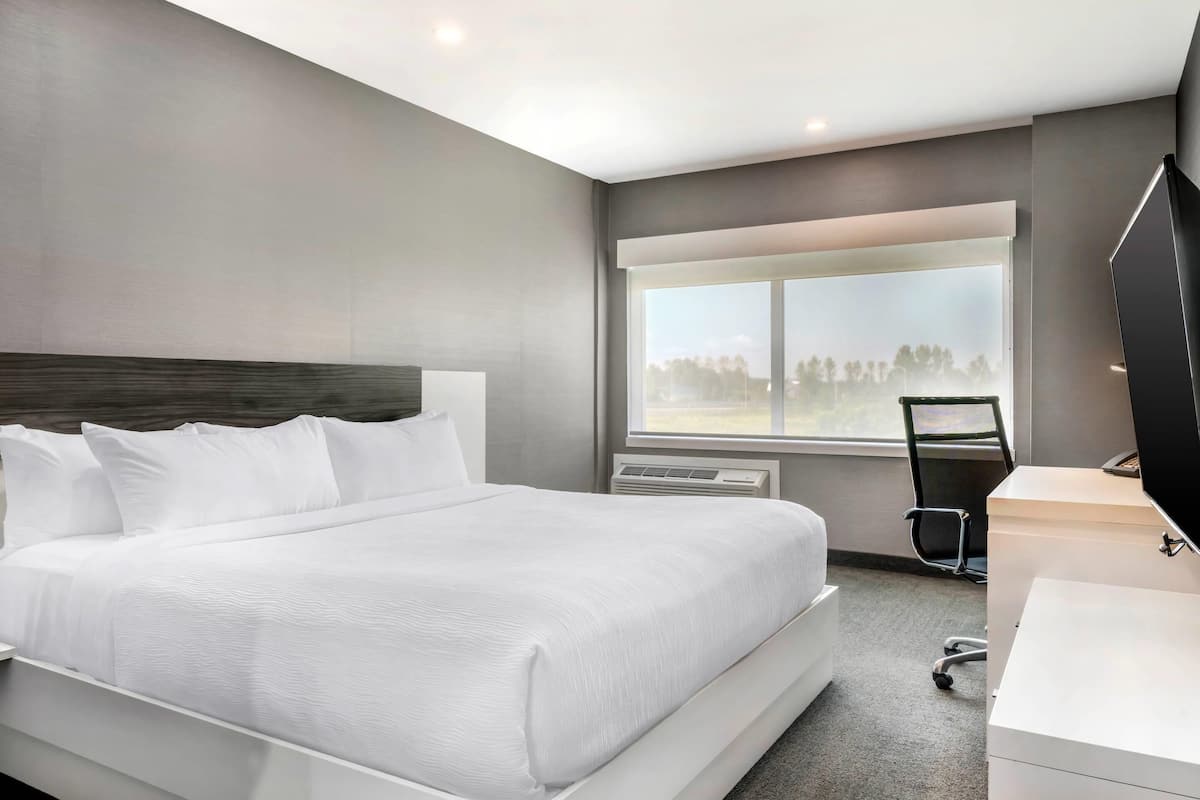 A modern hotel room with a large bed, a desk, a chair, and a TV.