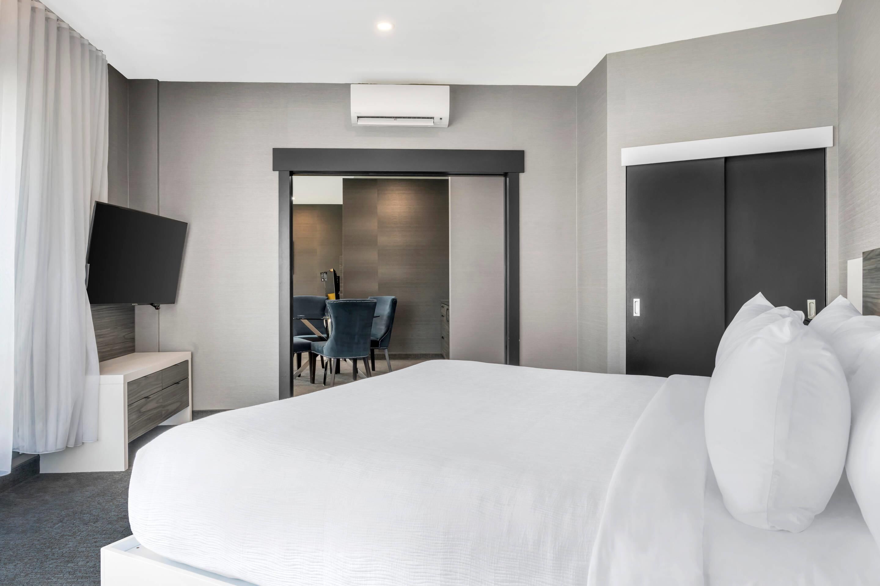 Moderni hotellihuone, jossa on suuri sänky, taulutelevisio, työpöytä tuolilla sekä vaatekaappi.