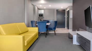 Un salon moderne avec un canapé jaune, une table à manger avec des chaises bleues, un téléviseur à écran plat et un four à micro-ondes en arrière-plan.