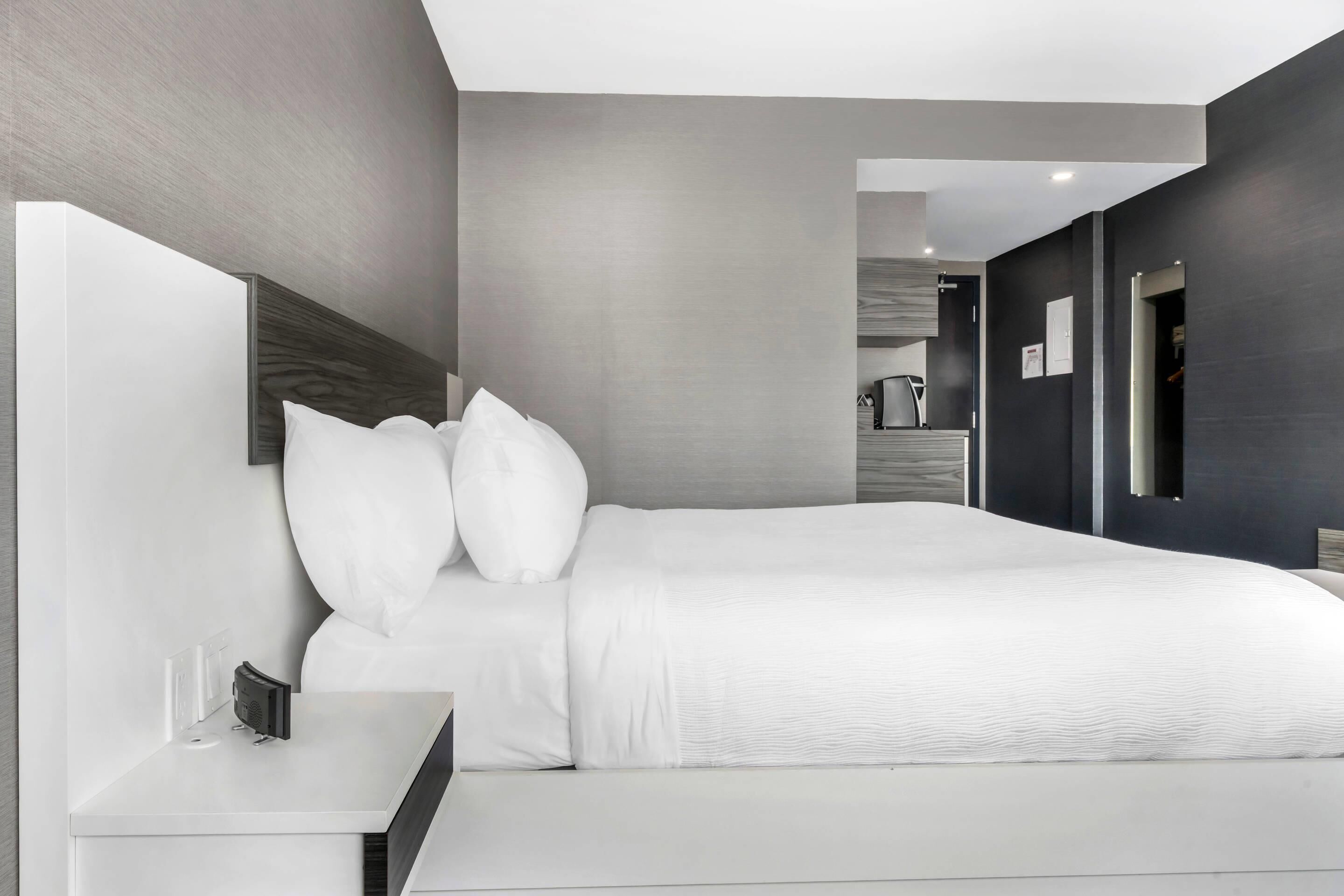 Una habitación de hotel moderna con una cama grande, una mesita de noche y un banco integrado.
