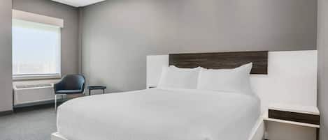 A modern hotel room with a large bed, a bedside table, a chair, and a window with a view.