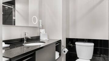 A modern bathroom with a black countertop, a white sink, a mirror, and a toilet.
