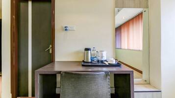 A hotel room with a wooden door, a small table with a water bottle, a thermos, cups, and a tray.