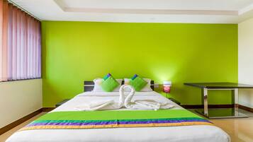 A hotel room with a bed, green walls, a window with curtains, a bedside table, and a lamp.