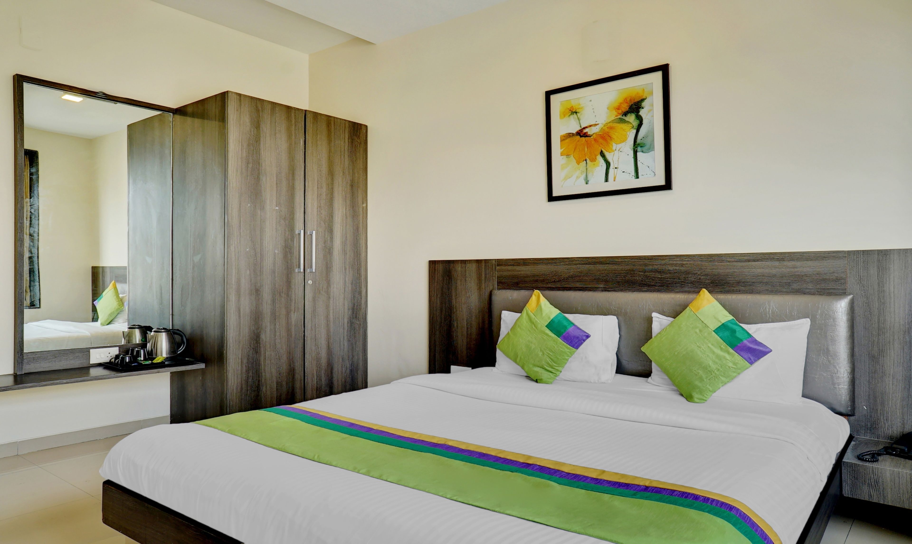 A hotel room with a large bed, a wardrobe, a bedside table, a telephone, and a painting on the wall.