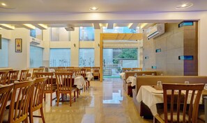 A restaurant with wooden chairs and tables, large windows, and an open doorway leading outside. - Treebo Bhagyashree Executive (Pune)