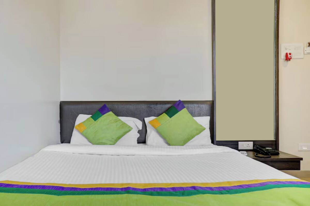 A hotel room with a bed, two pillows, a bedside table with a phone, and a mirror on the wall.