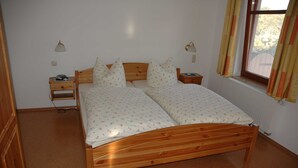 Una cama doble con ropa de cama floral, mesitas de noche con lámparas, una ventana con cortinas y un radiador.
