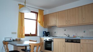 Una cocina con armarios de madera, una mesa de comedor con sillas, una cafetera y una ventana con cortinas.