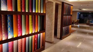 A hotel lobby with a colorful fabric display, a seating area with a sofa and chairs, and a reflective marble floor. - Hotel Le Lotus Grand Varanasi (Varanasi)