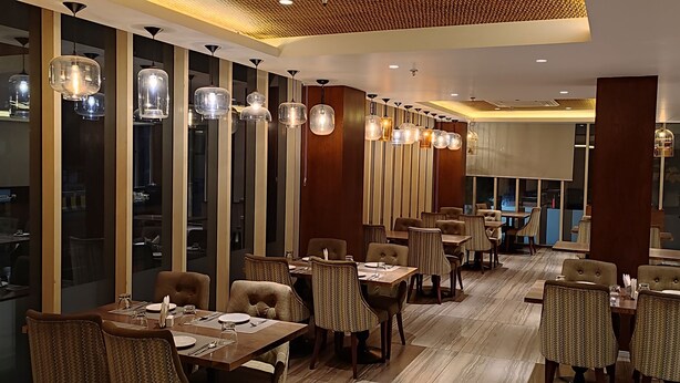 A modern restaurant with high ceilings, pendant lighting, and a view of the city through large windows. - Hotel Le Lotus Grand Varanasi (Varanasi)