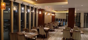 A modern restaurant with high ceilings, pendant lighting, and a view of the city through large windows.