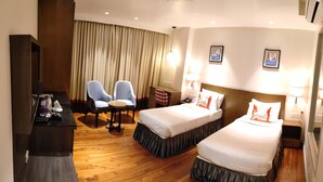 A hotel room with two beds, a desk, a chair, and a TV. - Hotel Le Lotus Grand Varanasi (Varanasi)