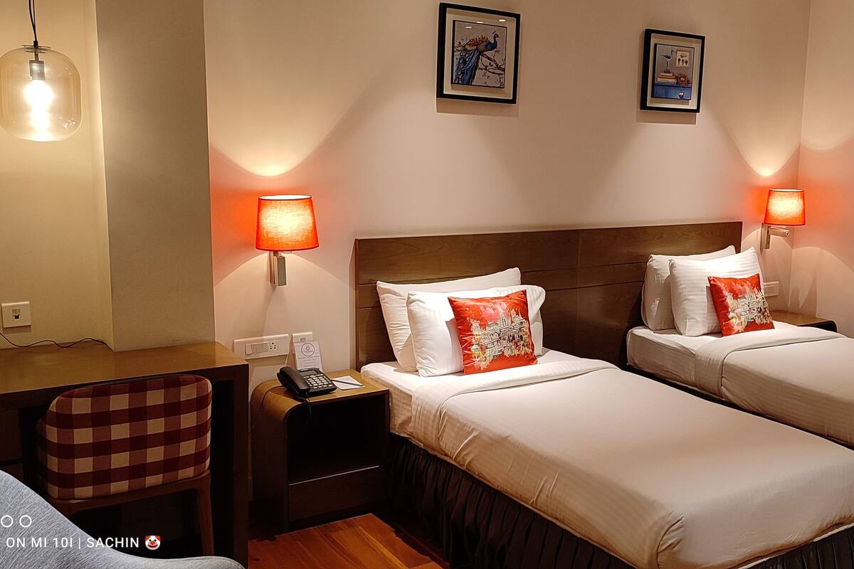 A hotel room with two beds, a desk, a chair, and a window.