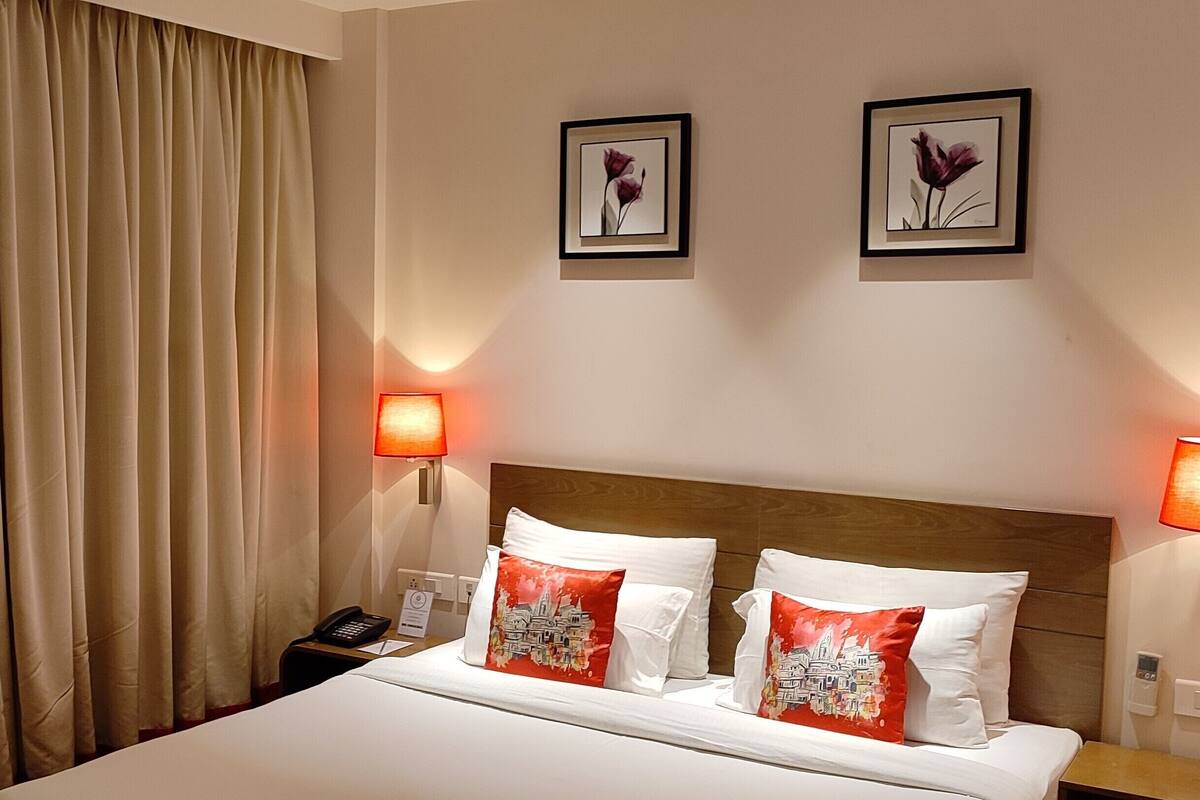 A hotel room with a large bed, two wall-mounted lamps, and two framed pictures on the wall.