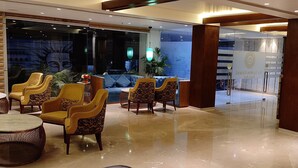 A lobby with a reception desk, seating area with chairs, and a glass partition. - Hotel Le Lotus Grand Varanasi (Varanasi)