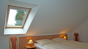 A bedroom with a skylight, a bed with pillows, a nightstand with a lamp, and a chair. - Sonnenhus Rügen 3 a few minutes to the beach central - Sonnenhus Rügen central (Sellin)