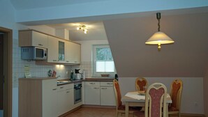 A kitchen with white cabinets, a microwave, a stove, and a dining area with a table and chairs. - Sonnenhus Rügen 3 a few minutes to the beach central - Sonnenhus Rügen central (Sellin)