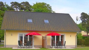 A two-story building with a tiled roof, two small windows, and a covered patio with chairs and a red umbrella. - Sonnenhus Rügen 3 a few minutes to the beach central - Sonnenhus Rügen central (Sellin)