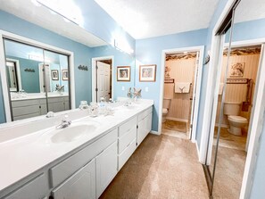 Un baño con un lavamanos largo, un espejo grande y una zona de ducha.