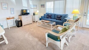 Ein Wohnzimmer mit einem blauen Sofa, Korbstühlen, einem Fernseher und einem Deckenventilator.