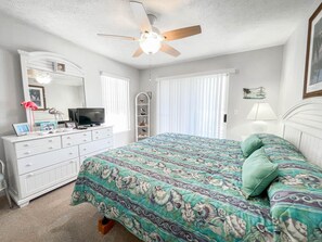 Un dormitorio con cama, cómoda, televisor y ventilador de techo.