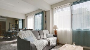 Ein modernes Wohnzimmer mit einem grauen Sofa, einem Holztisch und einem Essbereich im Hintergrund.