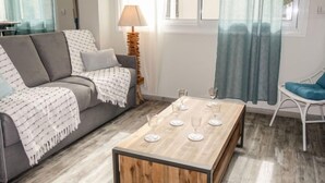 Ein modernes Wohnzimmer mit einem grauen Sofa, einem Holztisch mit Weingläsern, einem weißen Sessel und einer Lampe.