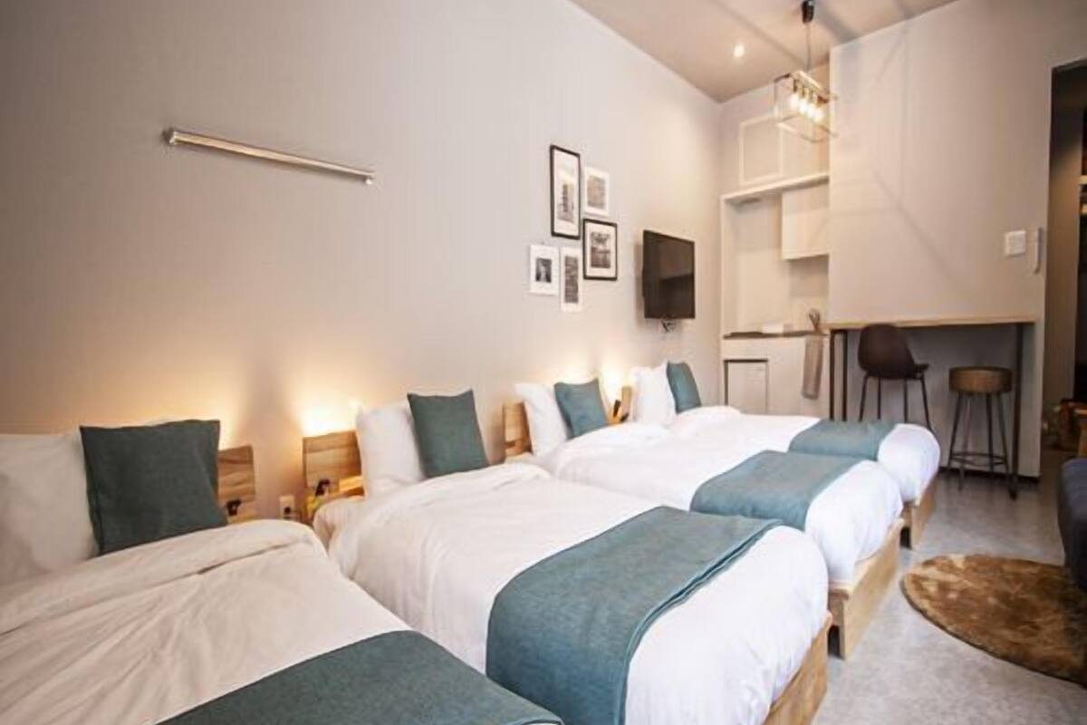 A hotel room with three beds, a desk, and a TV.